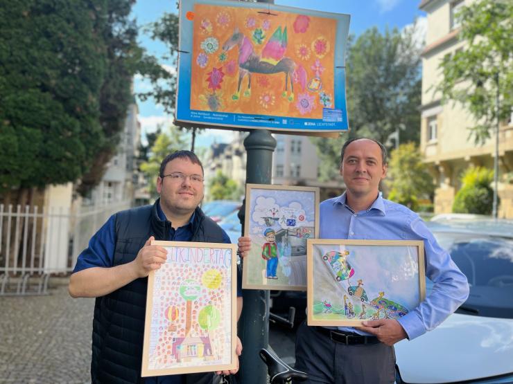 Zwei Männer zeigen Kunstwerke von Kindern