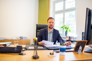 Oberbürgermeister Dr. Thomas Nitzsche sitzt am Schreibtisch in seinem Büro mit einem Dokument in der Hand