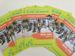 Mehrere Flyer der MUT-Tour liegen aufgefächert auf einem Tisch. Es ist ein Bild mit Fahrradfahrern zu sehen und der Termin in Jena.