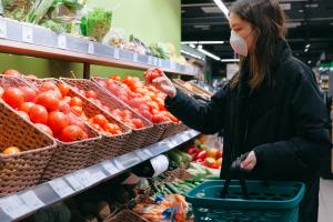 Frau kauft in einem Gemüseladen ein und hat eine Maske auf die Mund-Nase bedeckt.