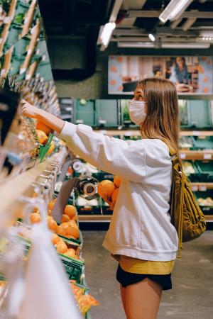 junge Frau mit Mund-Nasen-Bedeckung in einem Lebensmittelgeschäft vor einem Regal beim Einkaufen