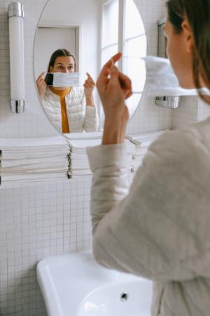 Junge Frau legt vor dem Spiegel eine Mund-Nasen-Bedeckung an