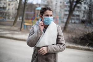 Frau mit Mund-NasenBedeckung steht vor Häuserblock