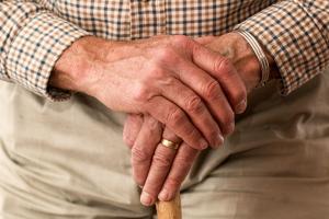 Zwei Hände einer älteren Person stützen sich auf einen Gehstock