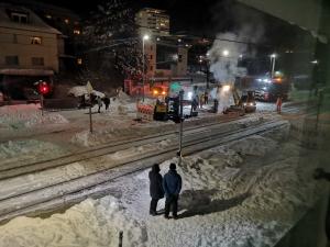 Blick auf die Kreuzung bzw. verschneite Straße im Dunkeln, zu sehen sind Arbeiter und Maschinen