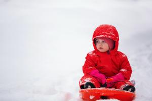 EIn Kind in einem roten Schneeanzug sitzt auf einem Schlitten