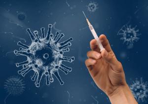 Hand hält eine Spritze, daneben das Coronavirus als blaue Kugel mit vielen Ausstülpungen in Großaufnahme