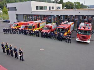 Etwa 30 Personen in Feuerwehrkleidung stehen vor 7 Feuerwehr-Fahrzeugen vor der Feuerwache Jena