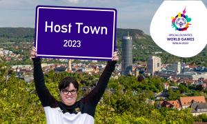 Frau in Sportsachen hält Jena-Schild hoch vor Stadtkulisse