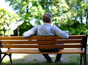 Ein älterer Mann sitzt auf einer Parkbank. Man sieht ihn von hinten.