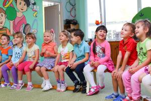 Lachende Kleinkinder sitzen im Kindergarten in einer Reihe