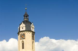 Ein Kirchturm mit Turmuhr vor blauem Himmel mit Wolken.