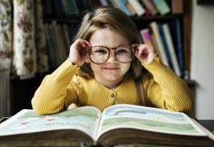 Ein Mädchen mit Brille sitzt an einem Tisch, vor ihr liegt ein großes, aufgeschlagenes Buch.