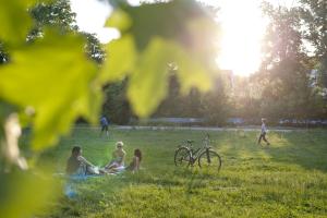 Eine Gruppe Frauen sitzten neben einem Fahrrad im Paradiespark Jena, Jugendliche spielen Ball. Es scheint die Sonne.