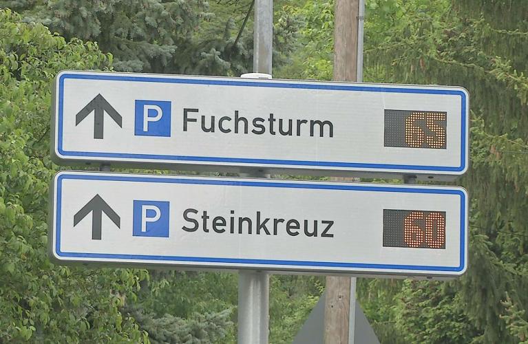 Zwei rechteckige weiße Schilder mit der Aufschrift Fuchsturm und Steinkreuz. Dahinter befindet sich die Digitalanzeige mit der Anzahl der freien Parkplätze.