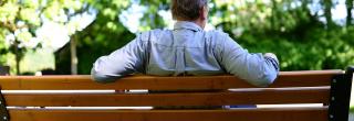 Ein älterer Mann sitzt auf einer Parkbank. Man sieht ihn von hinten.