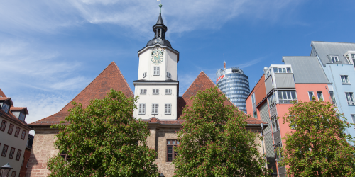 Blick auf das historische Rathaus vom Marktplatz aus, rechts daneben mehrere farbige Gebäude, im Hintergrund der Jentower