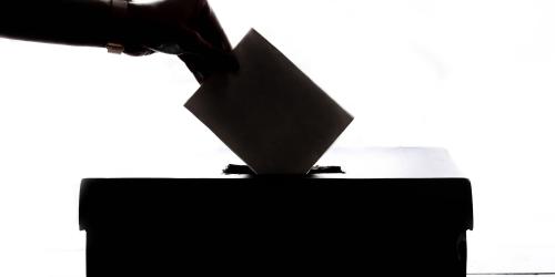 Eine Hand wirft einen Stimmzettel in eine Wahlurne ein.