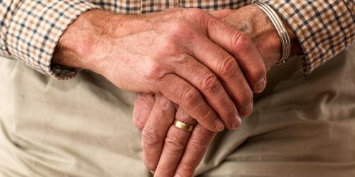 Zwei Hände einer älteren Person stützen sich auf einen Gehstock