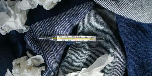 Ein Fieberthermometer und benutzte Taschentücher liegen auf Jeansstoff
