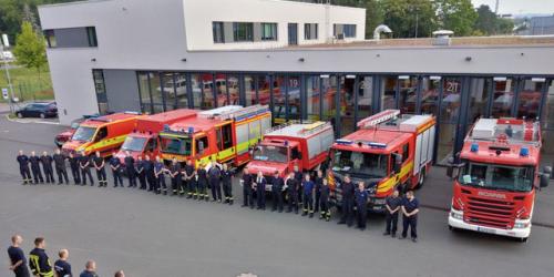 Etwa 30 Personen in Feuerwehrkleidung stehen vor 7 Feuerwehr-Fahrzeugen vor der Feuerwache Jena