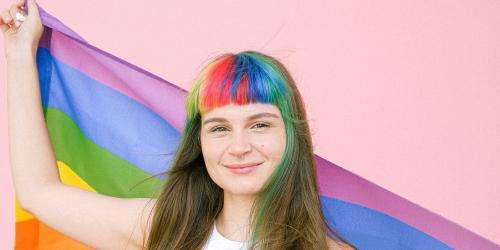 Eine Frau mit gefärbten Haaren hält eine Regenbogenfahne