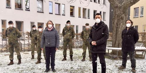 Menschen stehen in einer Schneelandschaft, darunter fünf Soldaten