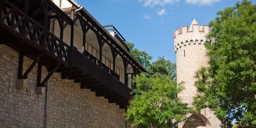 Eine hohe Mauer mit einem hölzernen Villengang und einem alten steinerenen Turm am Ende