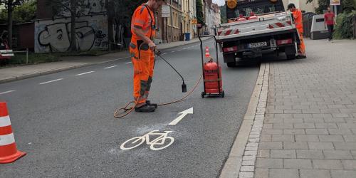 Ein Mitarbeiter vom Kommunalservice Jena bringt auf dem Magdelstieg ein Fahrrad-Piktogramm auf die Straße auf