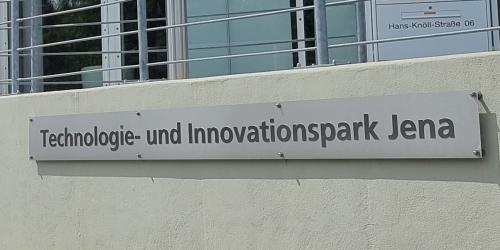 Blick ein Schild vor einem Gebäude mit der Aufschrift "Technologie- und Innovationspark Jena".