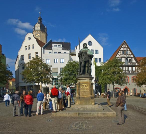 Eine Gruppe von Menschen stehen auf einem Platz neben einem Denkmal.
