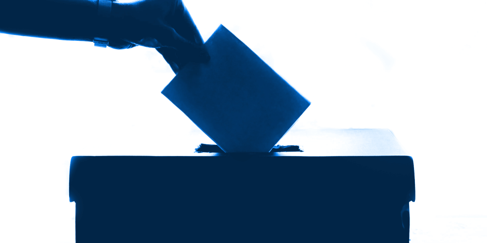 Eine Hand wirft einen Stimmzettel in eine Wahlurne ein.