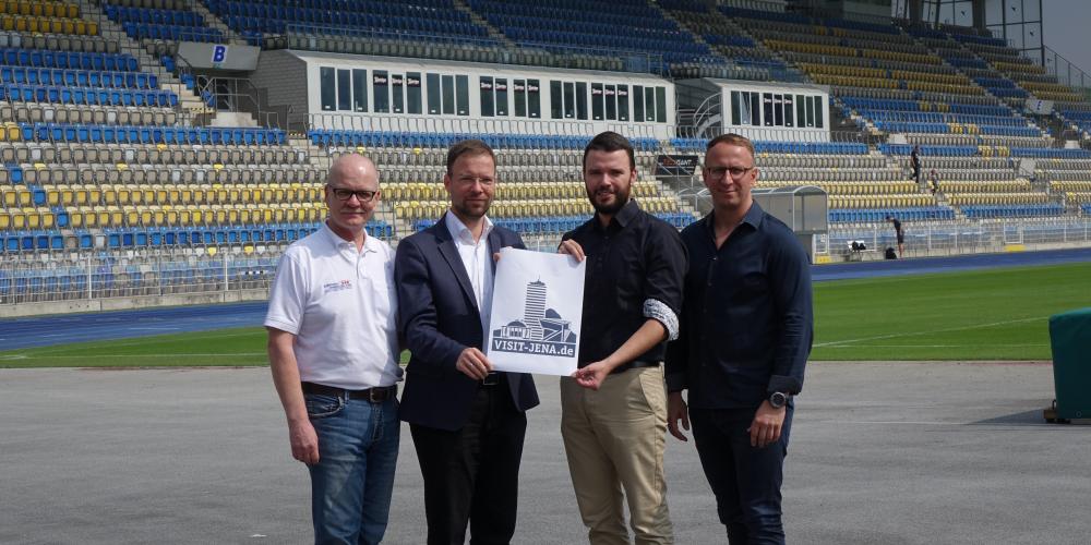 Karl-Hermann Kliewe, Dr. Thomas Nitzsche, Benjamin Koppe und Carsten Müller halten im Stadion einen Zettelmit dem neuen Logo