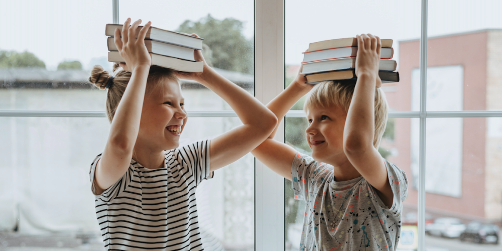 Zwei Kinder haben Bücher auf den Kopf und machen Faxen 