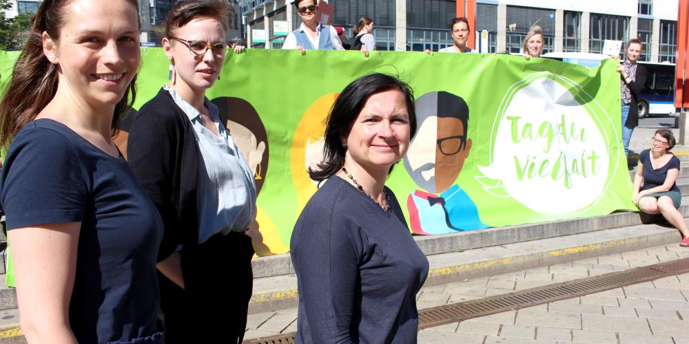 Drei Frauen stehen vor einem Plakat auf dem "Tag der Vielfalt" steht.