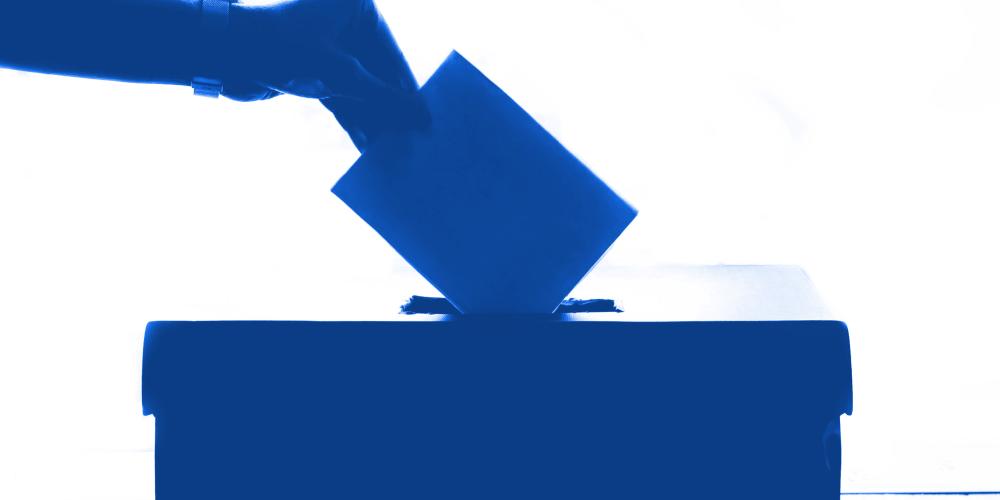 Eine Hand steckt einen Wahlzettel in die Wahlurne