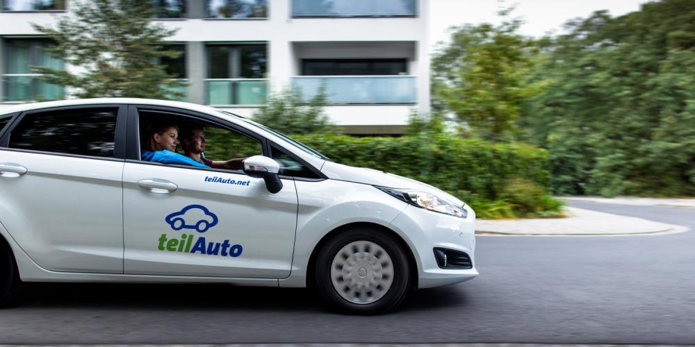 Ein Auto des Carsharing-Anbieters teilAuto fährt durch ein Wohngebiet