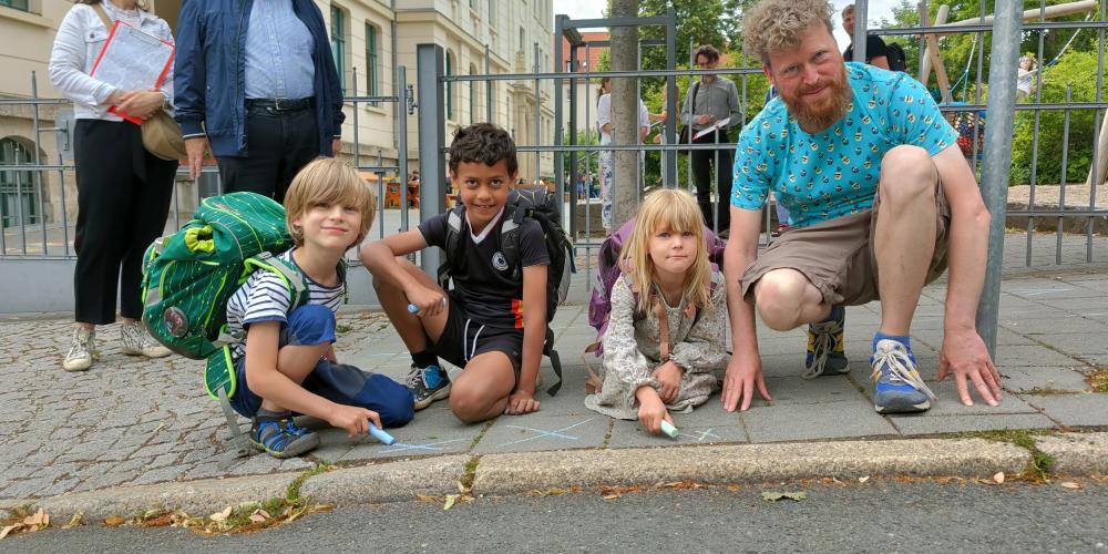 Die 7-jährigen Kinder Justus, Josef und Marla mit Erzieher Tino Buschbeck (v.l.) markieren ihren Schulweg mit Kreide. (Credit: Stadt Jena)