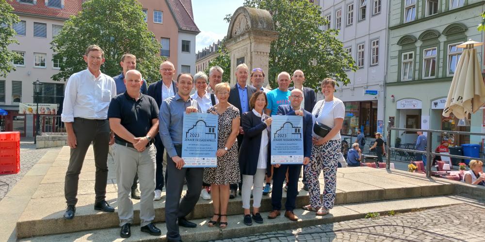 Bürgermeister Christian Gerlitz mit Sponsor*innen des Fassadenpreises stehen auf dem Jenaer Marktplatz am Brunnen.
