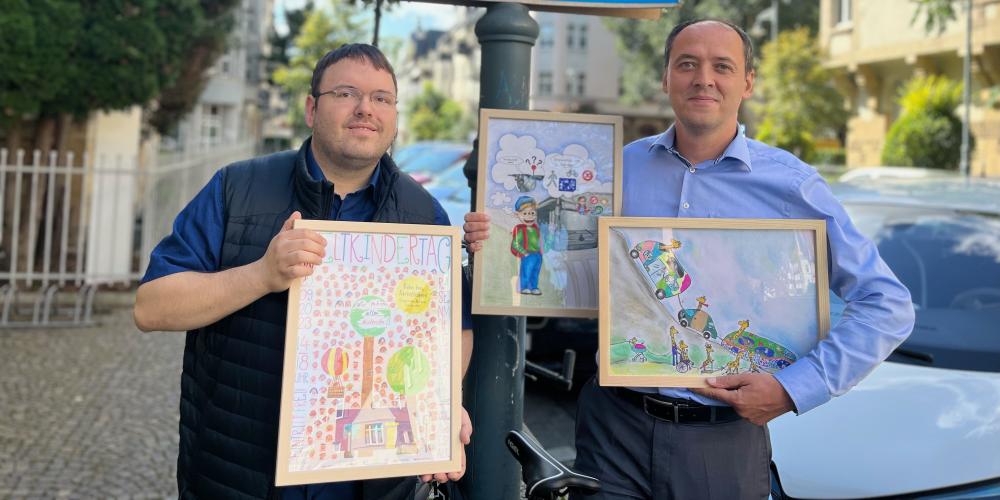 Zwei Männer zeigen Kunstwerke von Kindern