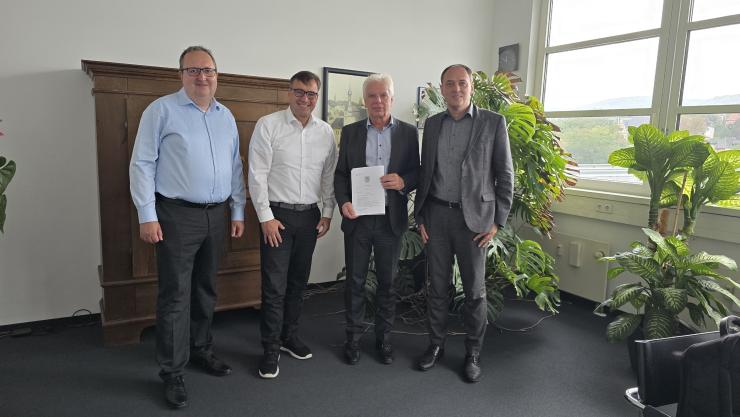 Vier Männer stehen in einem Raum und halten eine Notarurkunde in den Händen