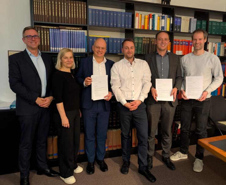 v.l.: André Sack, Claudia Budich, Tobias Wolfrum, Hermann Zebisch, Christian Gerlitz und Dr. Simon Münch stehen vor einem Bücherregal mit den unterzeichneten Vertrag