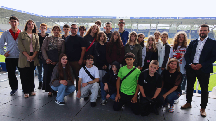 Viele Menschen schauen in der Fußballarena in die Kamera.
