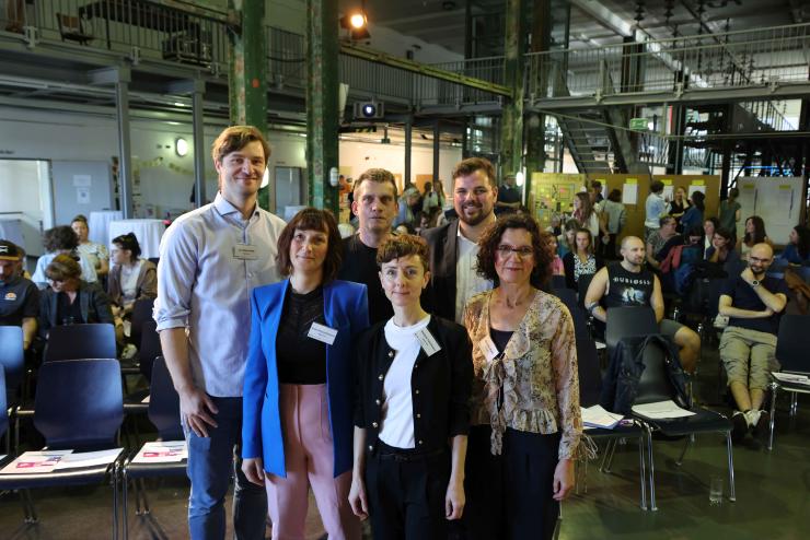 Mehrere Personen schauen in die Kamera, im Hintergrund mehrere Menschen.