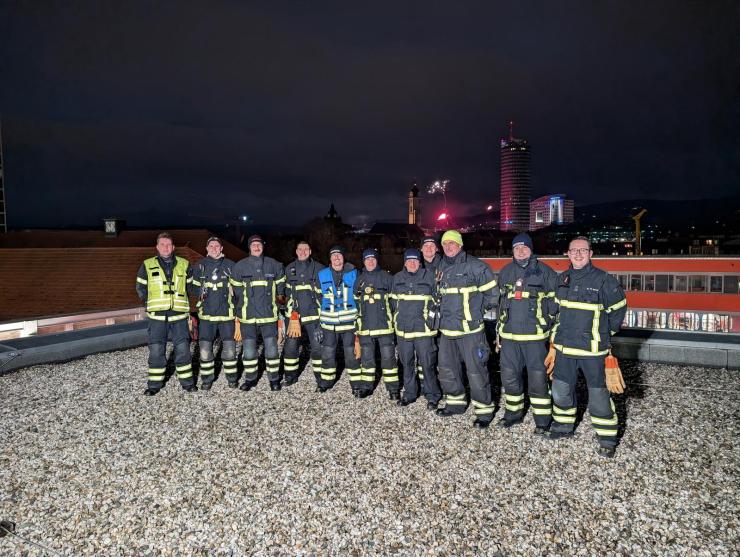 Mehrere Feuerwehrmänner schauen in die Kamera, im Hintergrund Feuerwerk.