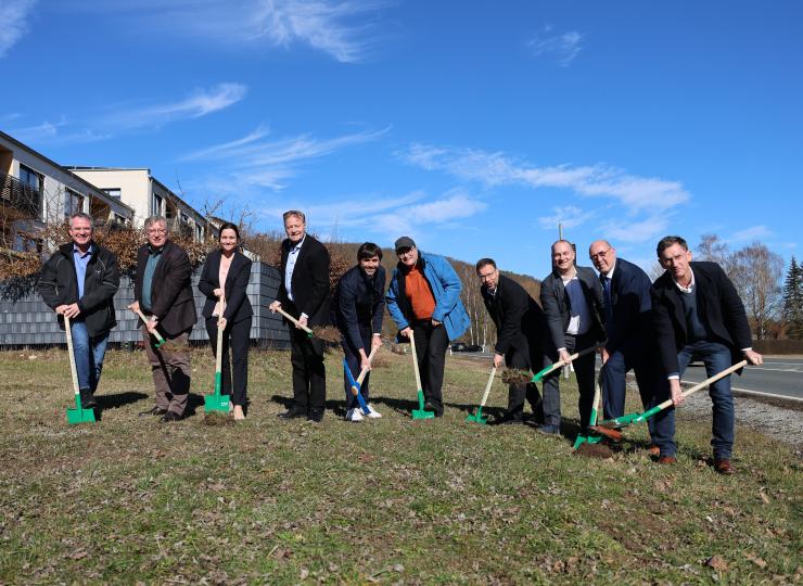 8 Männer und eine Frau stehen in einer Reihe mit einem Spaten bzw. Spitzhacke in der Hand für einen symbolischen Spatenstich.