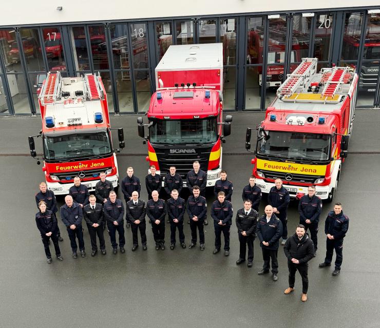 Feuerwehrleute stehen vor drei Autos und schauen in die Kamera.