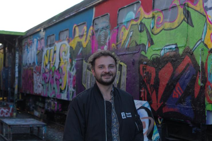 Ein Mann steht vor einer Mauer, auf der Graffiti aufgesprüht sind