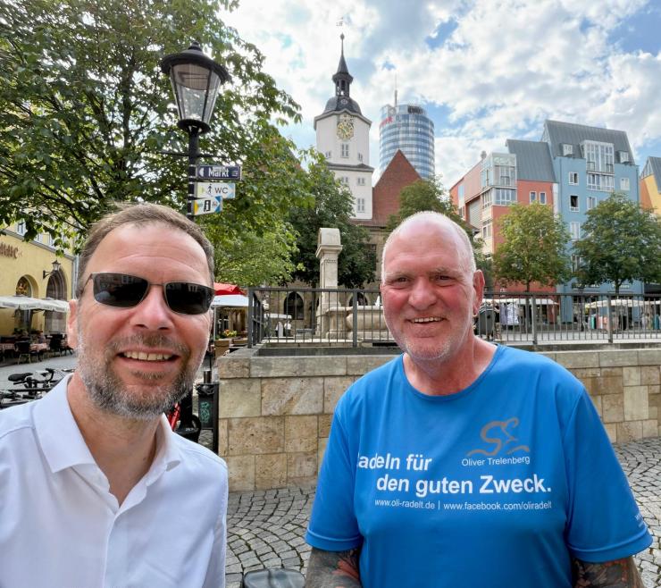 Zwei Männer stehen auf dem Markt in Jena und machen ein Slfie mit Rathaus und Jentower im Hintergrund
