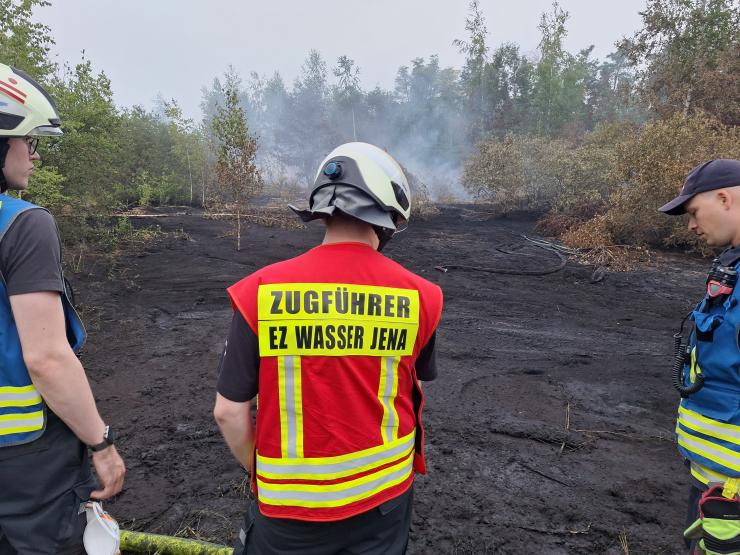 Einsatzkräfte sind von hinten zu sehen vor einer Brandfläche.
